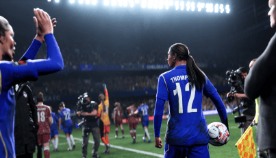 A football player wearing a blue number 12 shirt walks onto the pitch as photographers and fans welcome the new signing before a match.